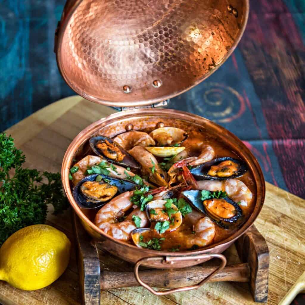 seafood stew in a copper pan on a wooden cutting board