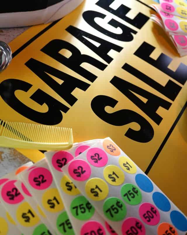 cool things to do in Wisconsin in May, Close up shot of a sign saying "Garage Sale" with some sheets of stickers in different bright colors with prices in dollars printed on them