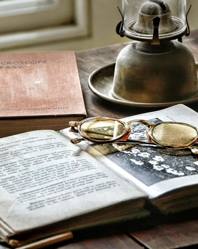 Close up shot of a wooden desk with a pair of round glasses resting on an old open book with another closed book and a gas lamp nearby in sheboygan, wisconsin