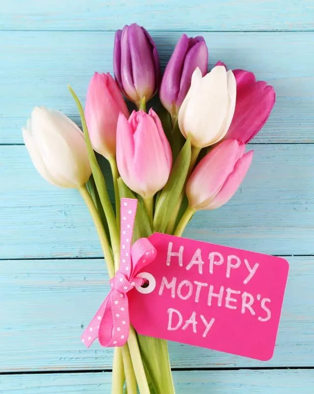 fun things to do in Wisconsin in May for Mother's Day, Bunch of flowers in shades of pink and purple all bunched together with a pink ribbon and a label saying "Happy Mother's Day" resting on a blue wooden table