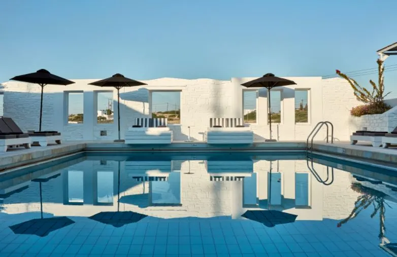 a ppool with a reflection of pool umbrellas and pool beds, with a white wall on a bright day