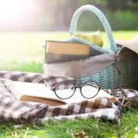 a basket with book in a field of grass on a picnic blanket with another boo and glasses