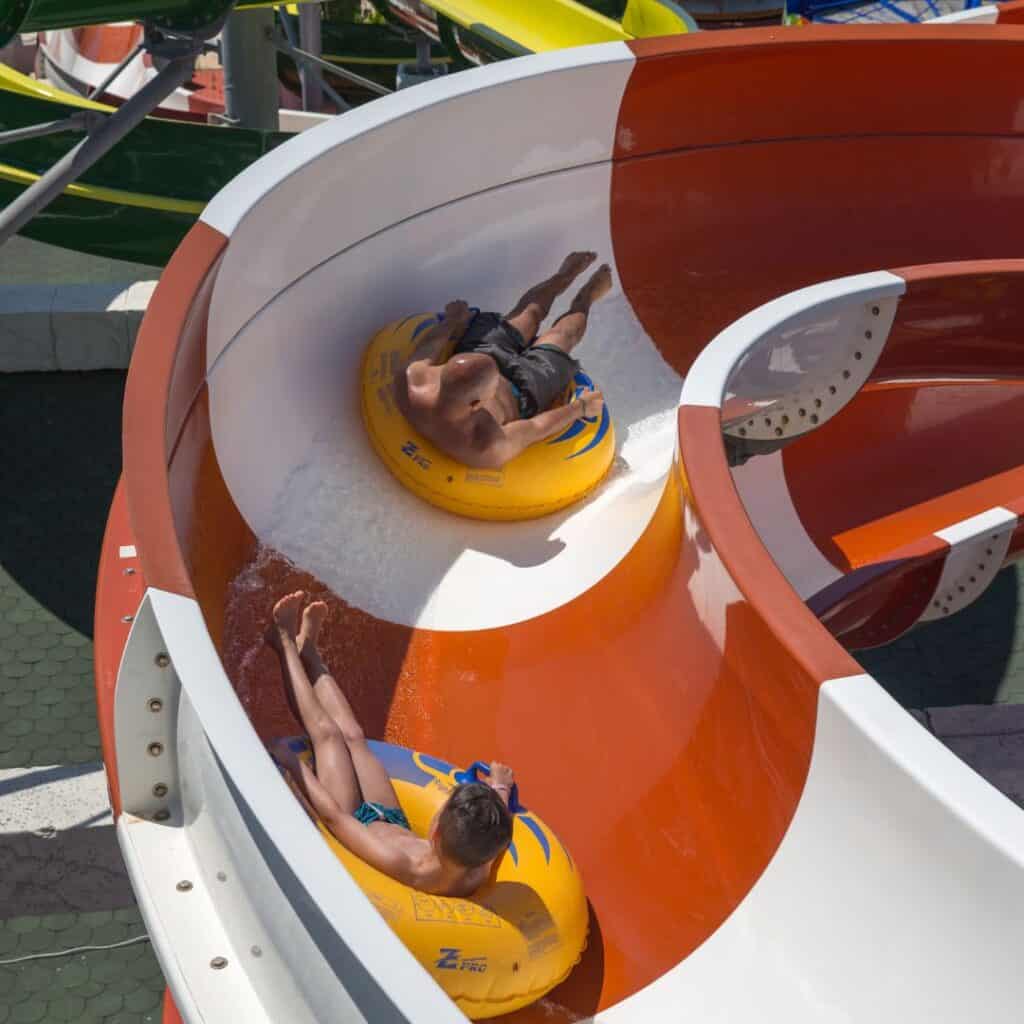 Two persons sliding down a colorful white and orange water slide