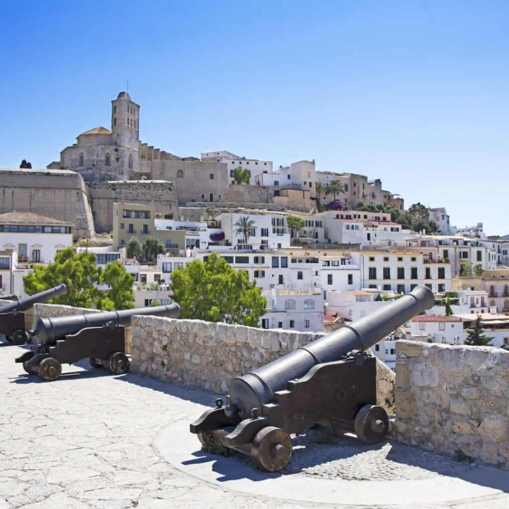 cannons on the wall of a town with a castle and white houses in the background