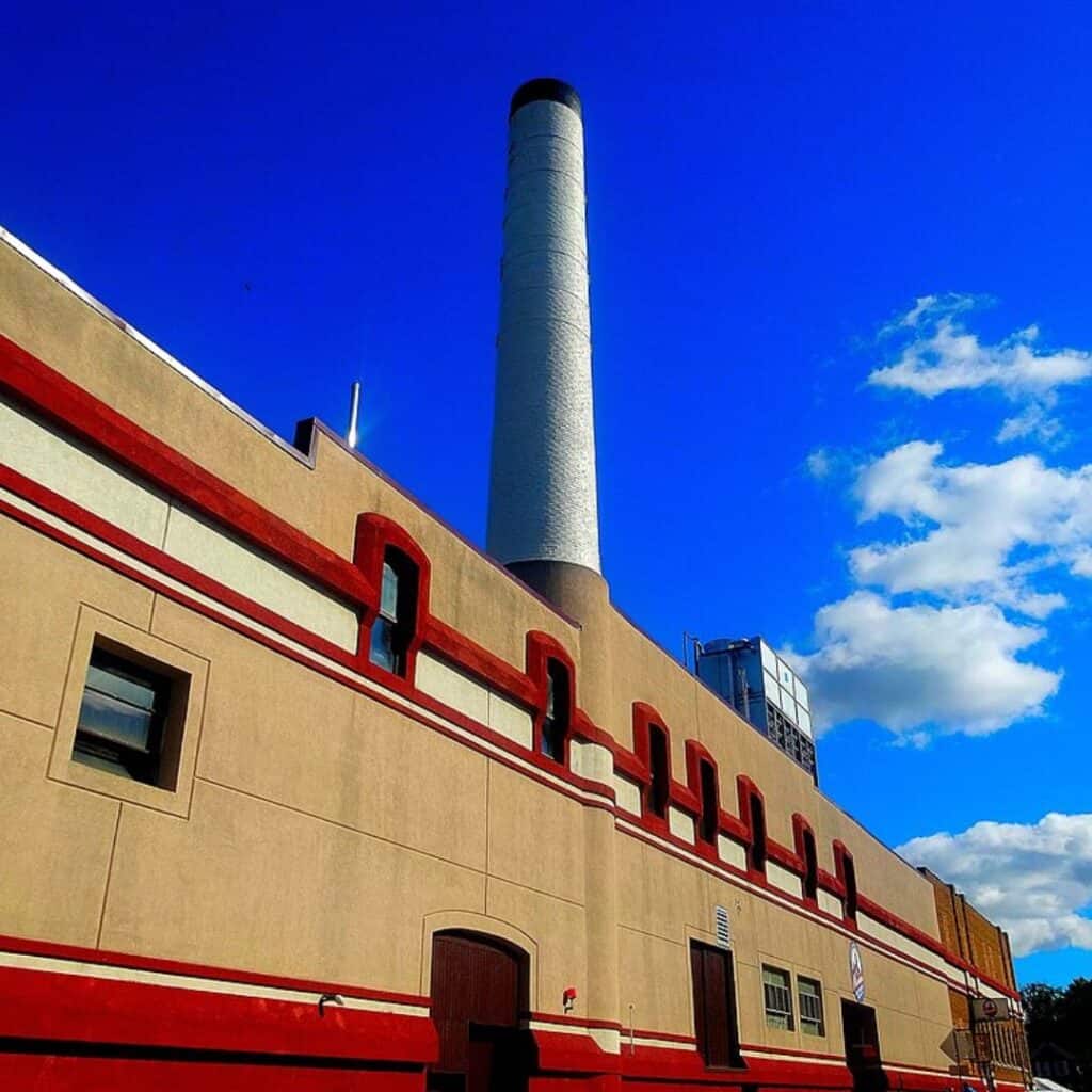 a red and white building with a large chimney and blue skies with clouds