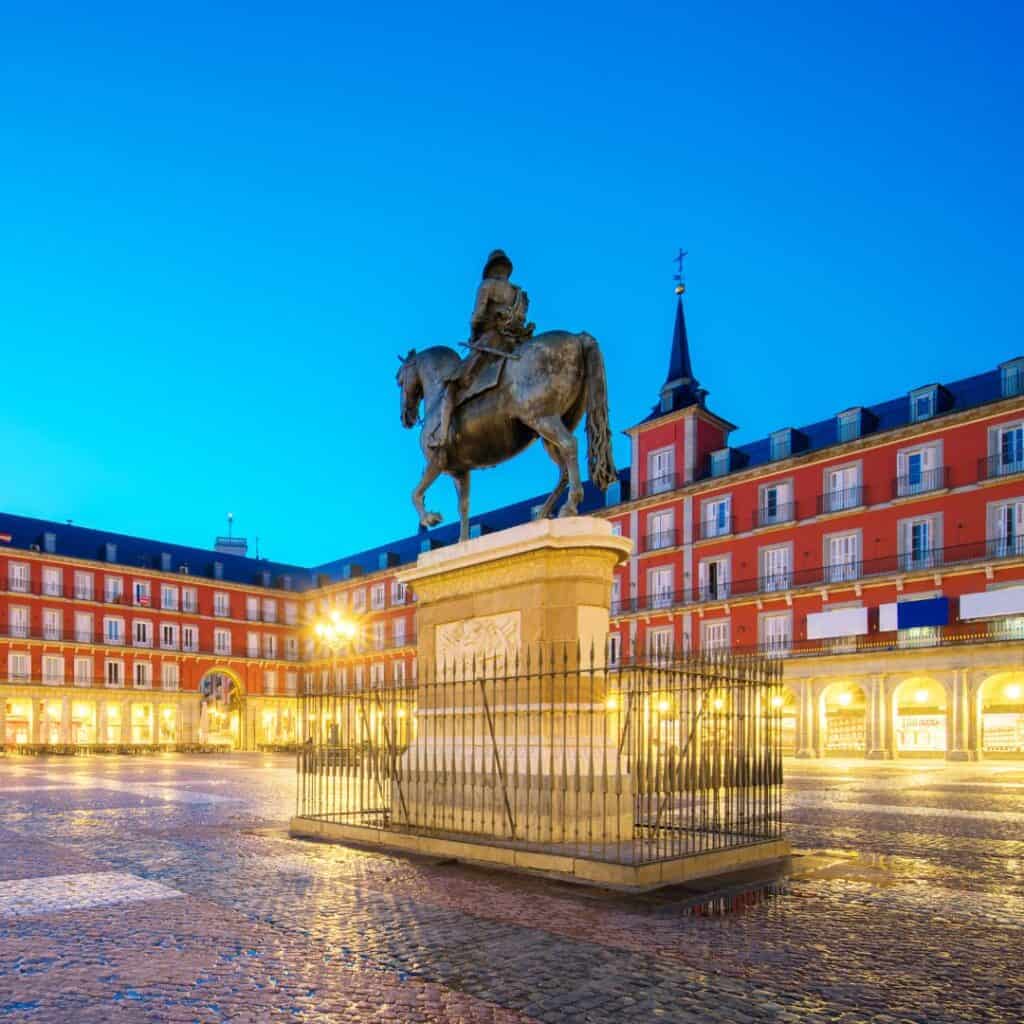 a statue of a person on a horse in front of a red building on plaza mayor in madrid