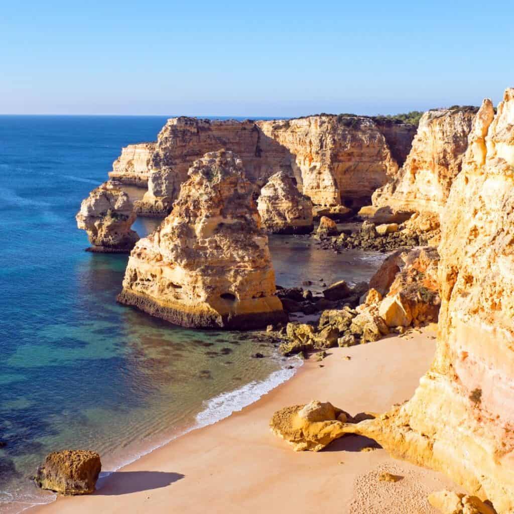 towering rocky cliffs with long strip of beach in praia de marinha, top things to do in algarve in may