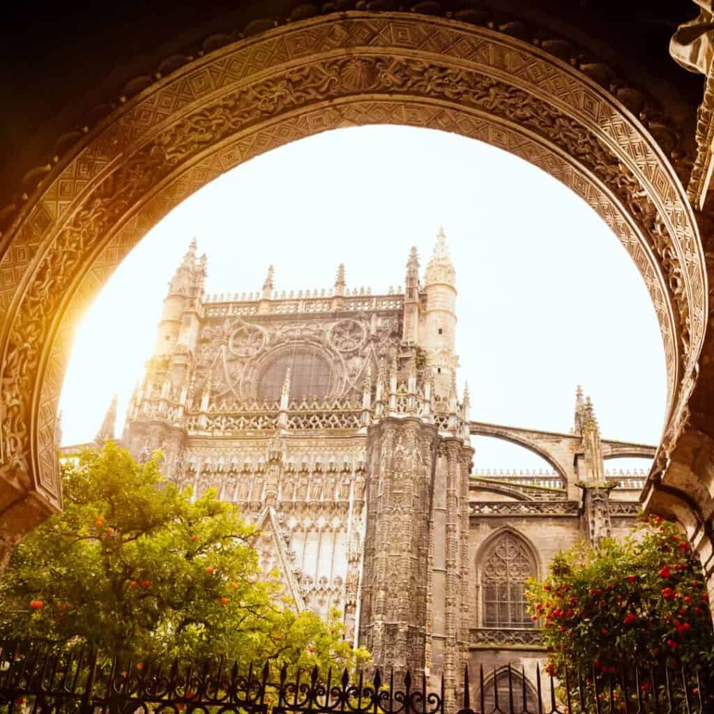 the sun shining through an archway in front of the Seville cathedral