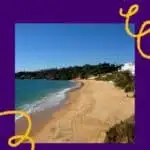 Pinterest pin about things to do in Albufeira in May, a long stretch of sandy beach with no people, green shrubbery, and blue waters in a clear sunny sky