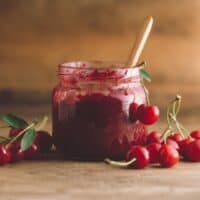 cherry jam in a glass jar beside fresh cherries on a wooden table