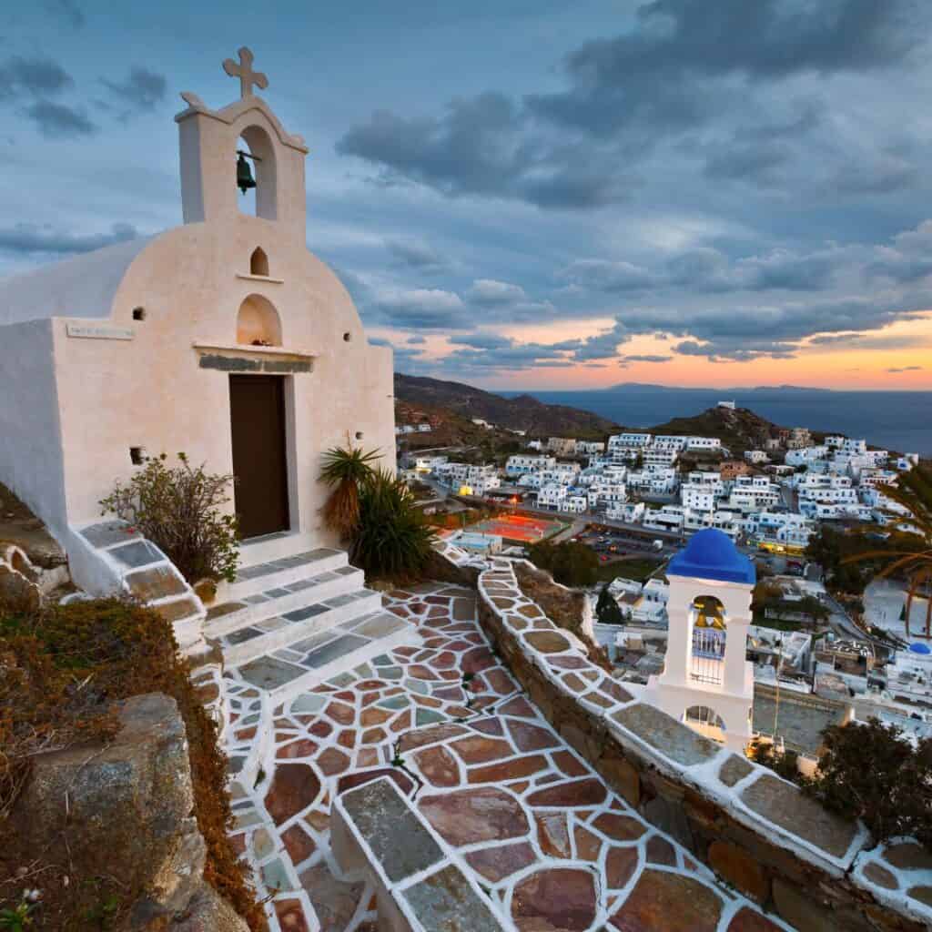 a view of a church with a tiled pathway and the town below with white-washed houses on the evening