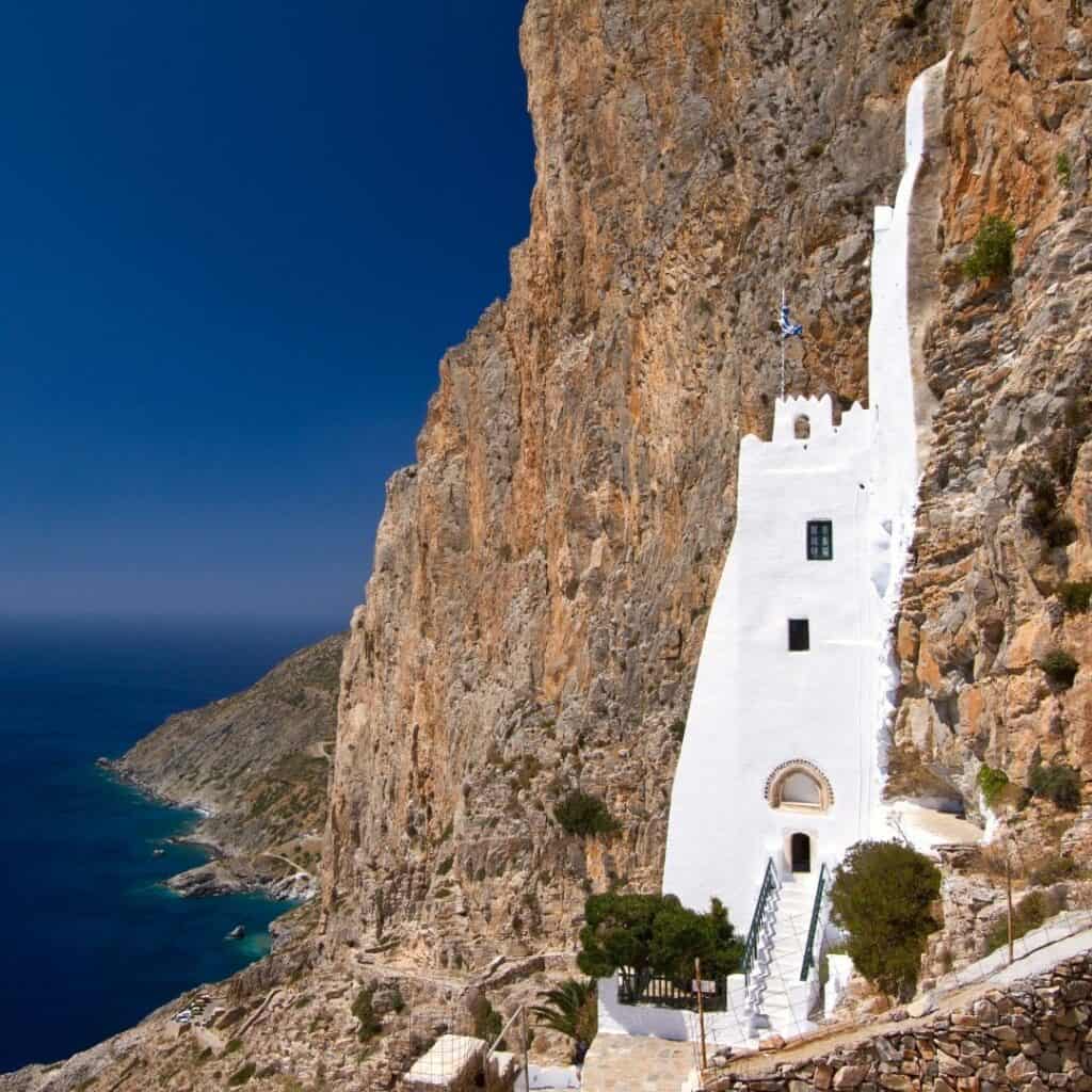 a white monastery on the side of a cliff overlooking the sea