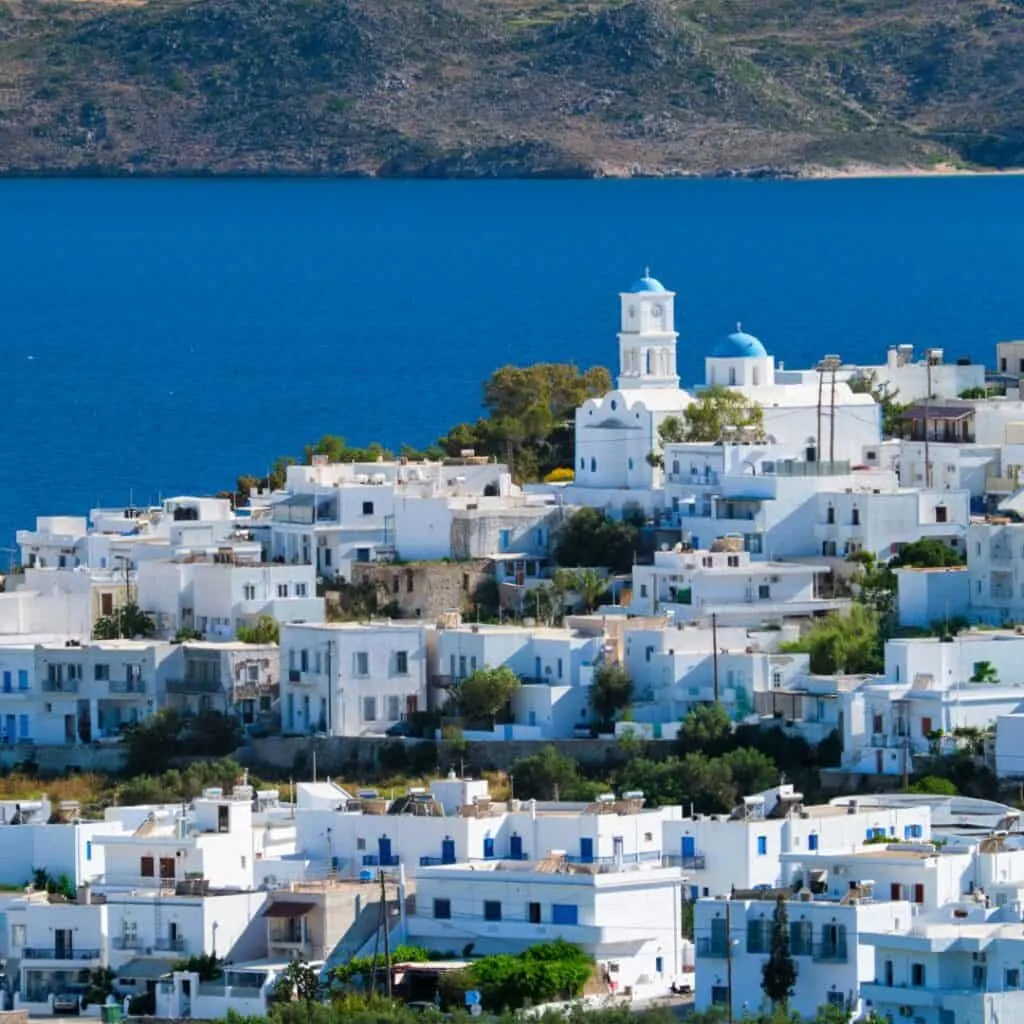 a village filled with white-washed houses on a hill with the sea and mountains as a background on a bright day