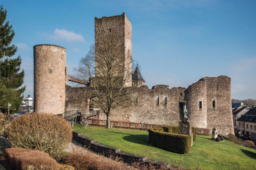 Exterior shot of Useldange Castle in Luxembourg with blue skies and gardens in a sunny day
