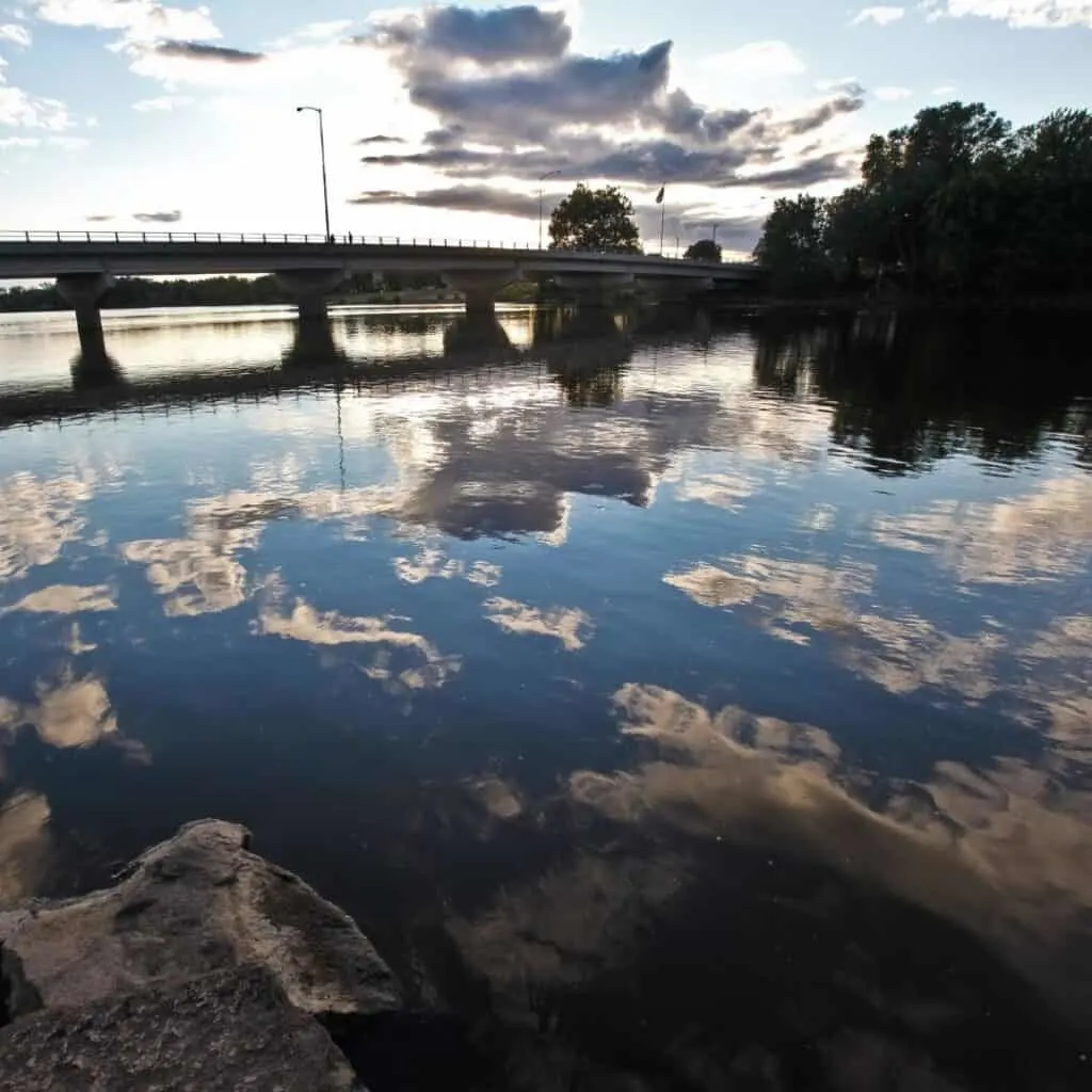 sky with clouds, a bridge, and trees reflected in the water of a river
