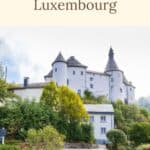 Pinterest pin about best castles in Luxembourg showing photo of clervaux castle with green foliage during a clear day