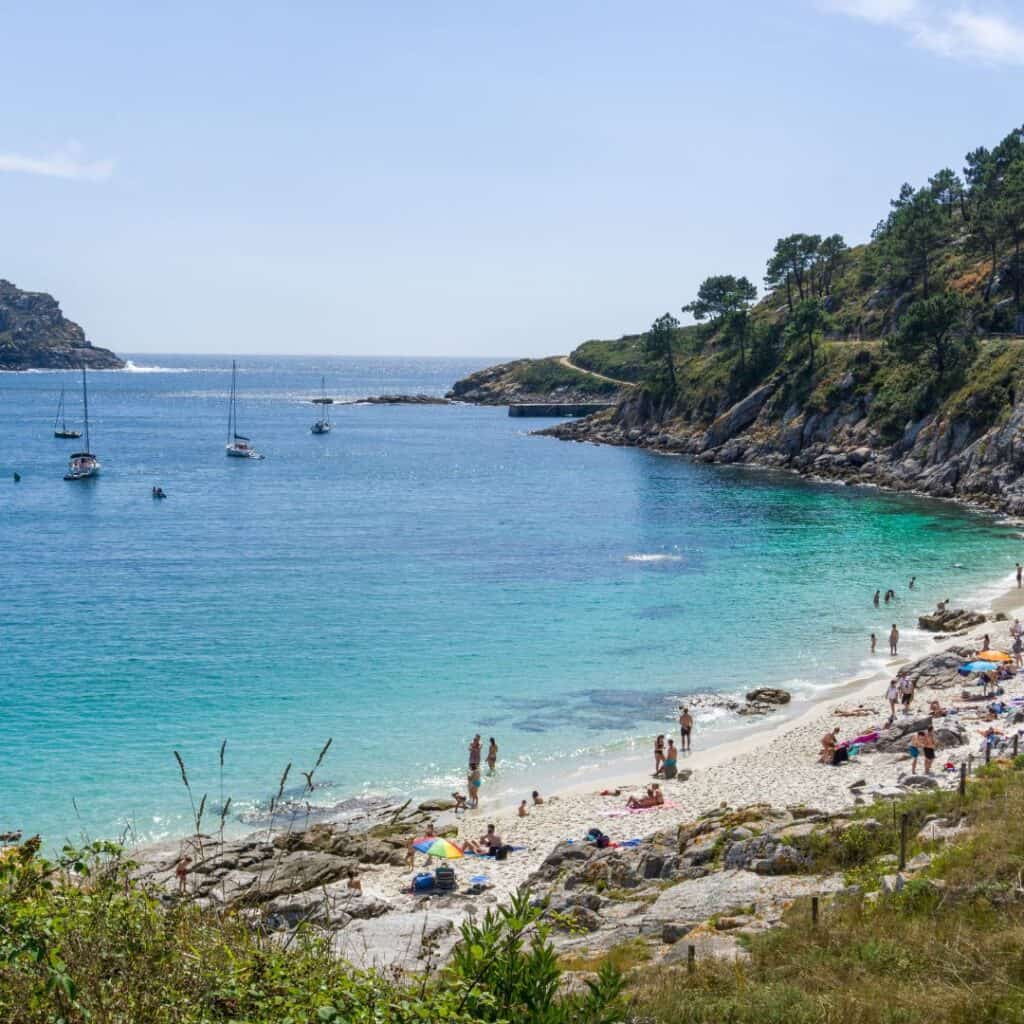 Scenic view of blue waters, white sand, people, and boats in Cíes Islands, spain