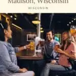 a group of people sitting together on a table toasting with beer at a bar