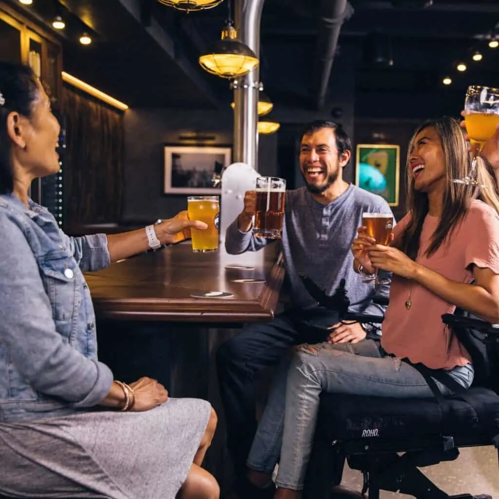 a group of people sitting together on a table toasting with beer at a bar in one of the breweries in Madison