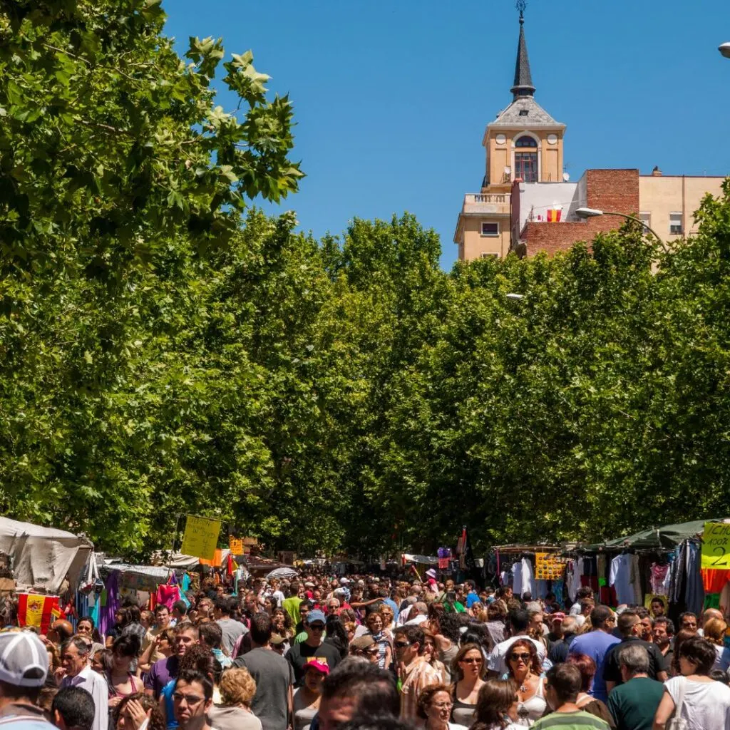 Crowds of people exploring and buying at El Rastro flea market in Madrid, Spain with a bright, blue sky above