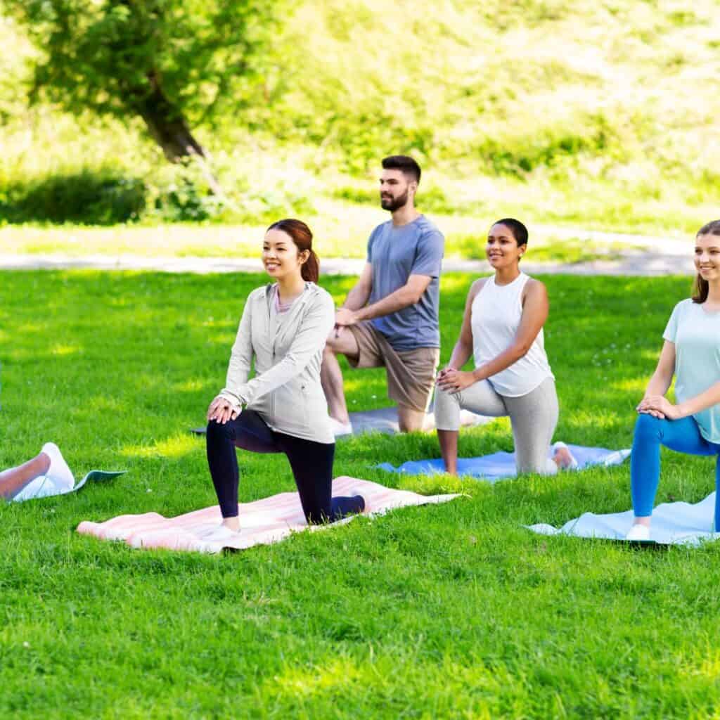 group of happy people doing yoga in park during summer in madrid