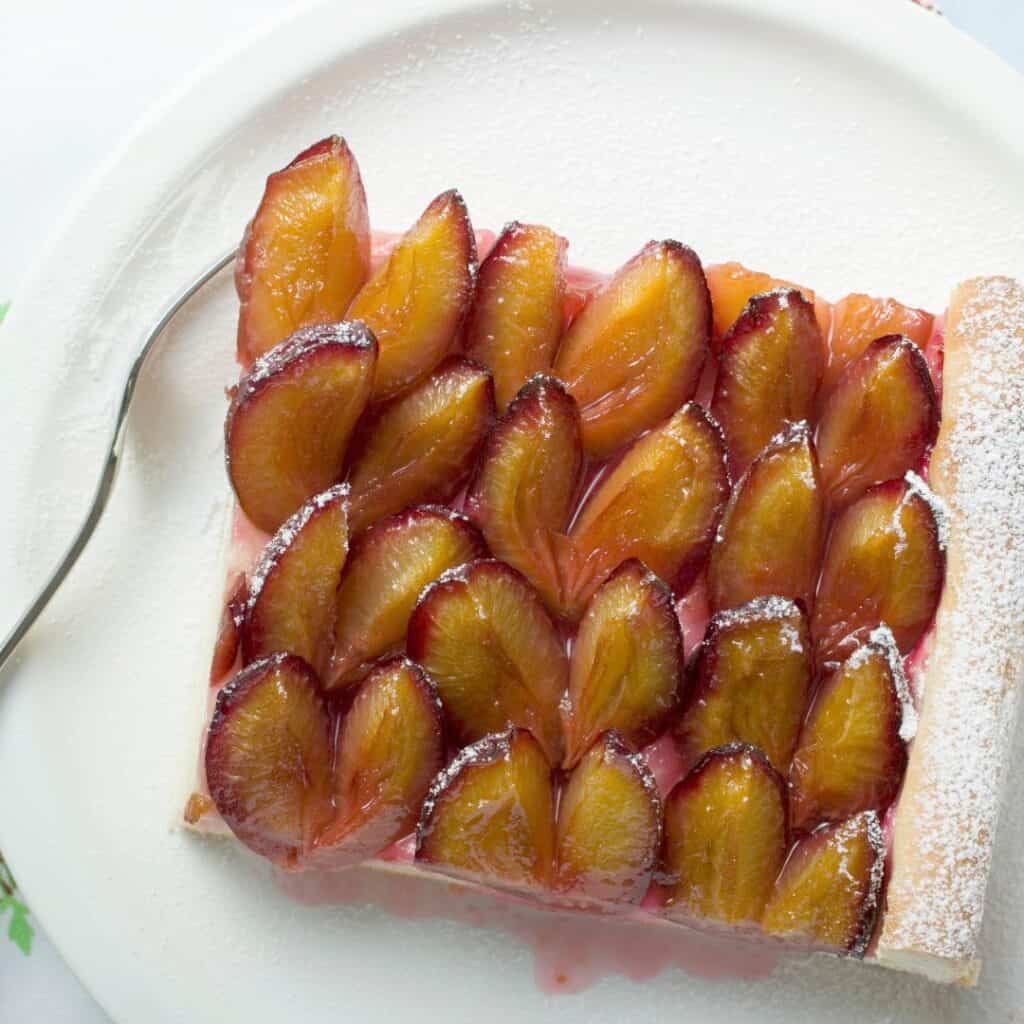 Quetschentaart slice served in white plate with fork. Damson plum tart. Traditional Luxembourg desserts.