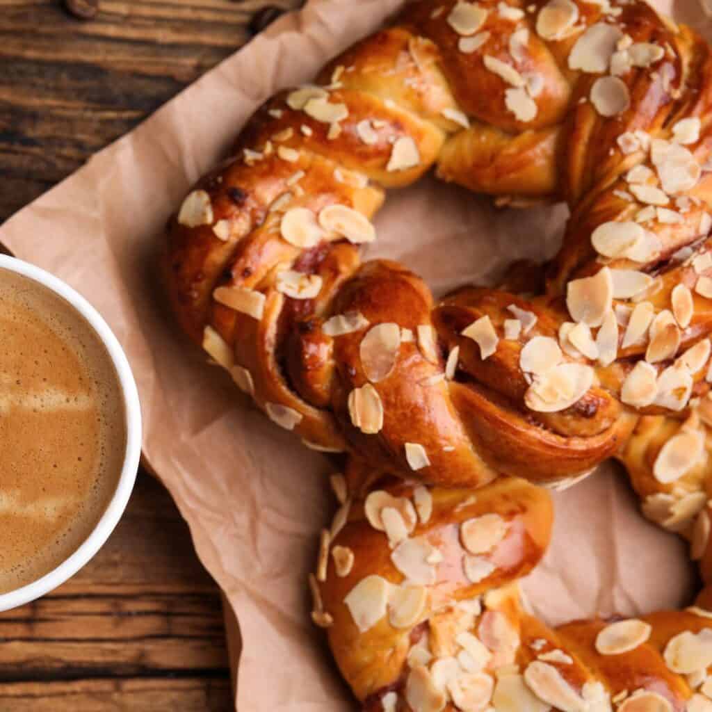 soft bretzel bread with almonds and cup of coffee in wooden table flatlay