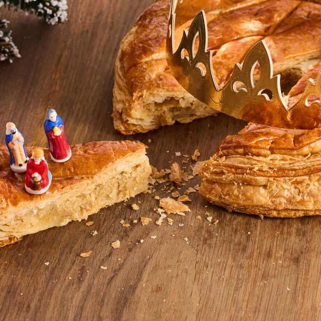 Dräikinnekskuch or three kings cake with gold crown and three small figurines in wooden table. Traditional Epiphany cake.