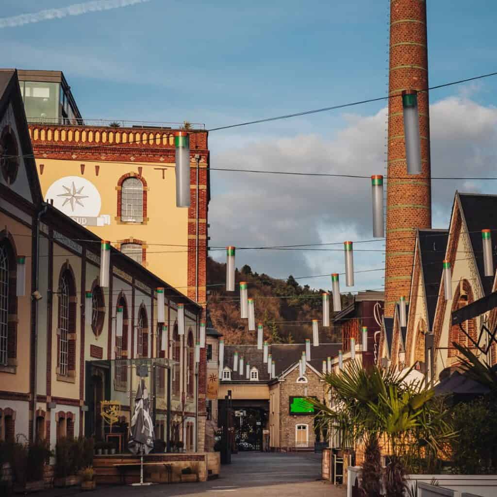 Photo of a row of colorful buildings with a tall chimney in the Clausen district of Luxembourg City. In the background, there are modern buildings of the European quarter.