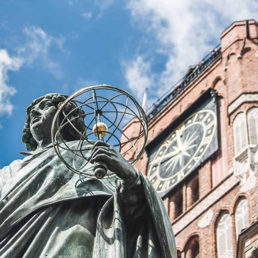 view from below of Nicolaus Copernicus Statue and a clock tower at the back and the sky