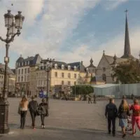 Photo of Place Guillaume II, featuring a equestrian statue of Grand Duke Guillaume II in the center. The surrounding area is filled with trees and people shopping, which is one of the fun things to do in Luxembourg City. In the background, the towers of the Cathédrale Notre-Dame can be seen.