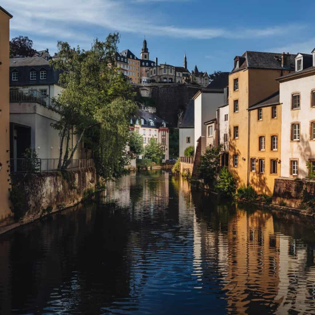 Afternoon view of the Grund neighborhood in Luxembourg City, featuring the Alzette River winding through the historic district with colorful facades lining the waterfront