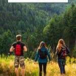 Pinterest pin about hiking in Luxembourg showing photo of three hikers standing in grassy hill taking in the mountain view