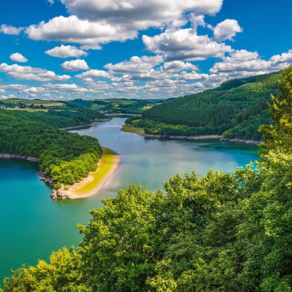 A scenic overlook from the Belvédère viewing platform offers a panoramic view of the Upper Sûre Lake, surrounded by trees, while hiking Nature Discovery Path Burfelt