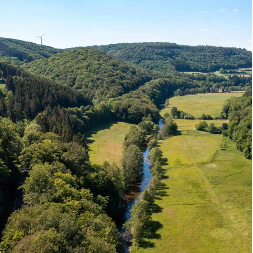 Aerial view of the Our River winding through a green valley in Naturpark Our, a Luxembourg bucketlist.