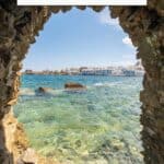 A Pinterest pin about Paros Greece Instagram spots featuring a photo of a scenic view of a coastal town framed by a natural rock archway.