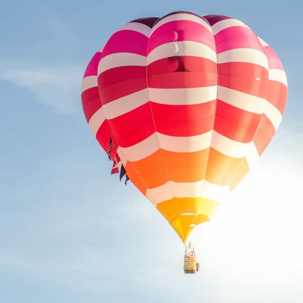 a colorful hot air balloon is flying in the sky being hidden in the sun