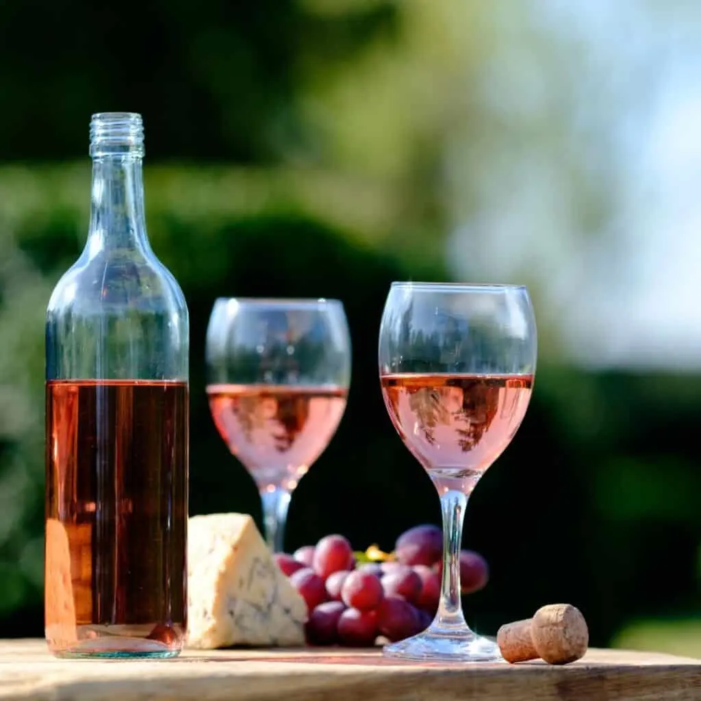 two glasses and a bottle of rose wine on a wooden table