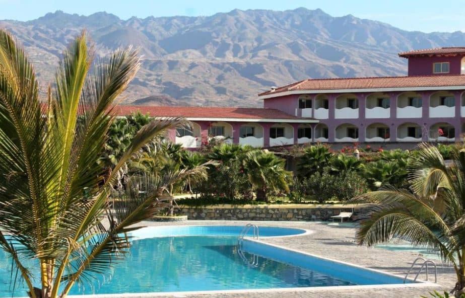 pool area surrounded by plam trees and hotel with the mountain in the back at Hotel Santantao Art Resort in Porto Novo, Cape Verde