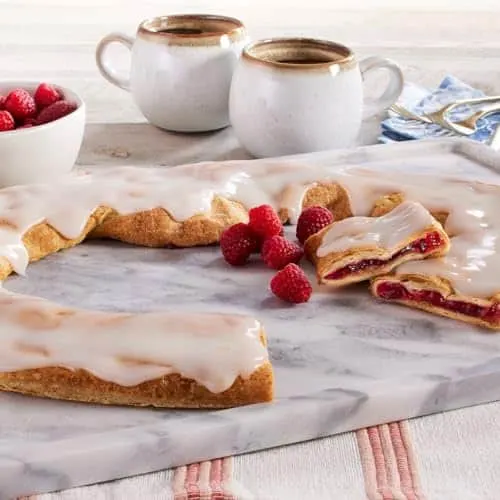 a pastry with icing and raspberries on it near tea cups