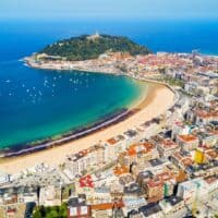 Aerial view of San Sebastian, Spain, featuring a beautiful bay with a sandy beach, a hilltop monument, and colorful buildings. One of the most unique places to visit in Northern Spain.