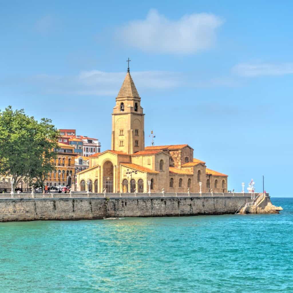 The Church of San Pedro in Gijón, Spain, a historic church located on the coast with a steeple and beautiful ocean views.