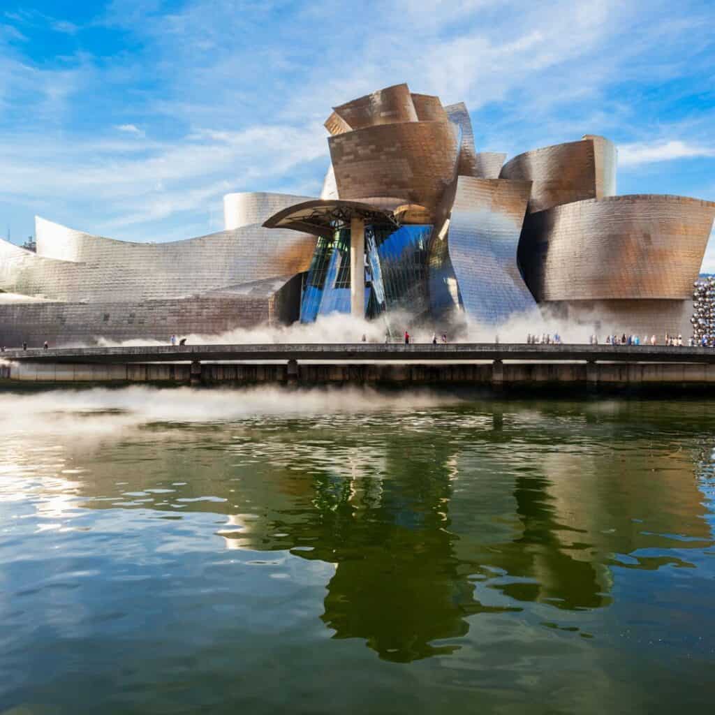 The Guggenheim Museum Bilbao, a modern art museum in Bilbao, Spain, with a unique, fluid architectural design reflected in the water below.