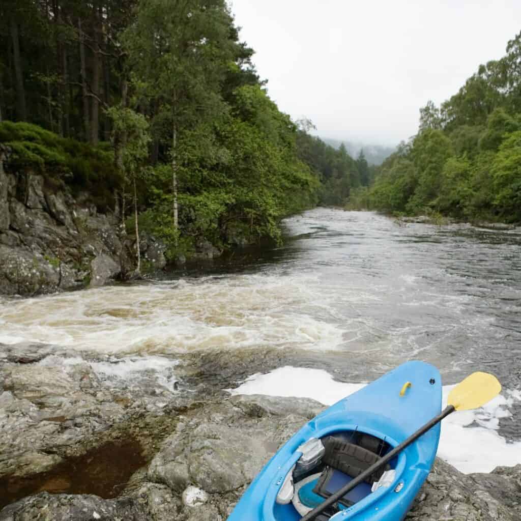 a blue kayak sits on the rocks next to a river