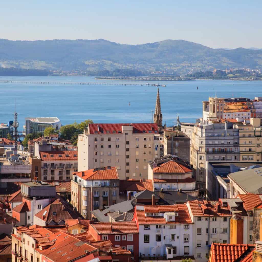 An aerial view of Santander, Spain, showing a cityscape with red-tiled buildings, a large body of water, and mountains in the distance.