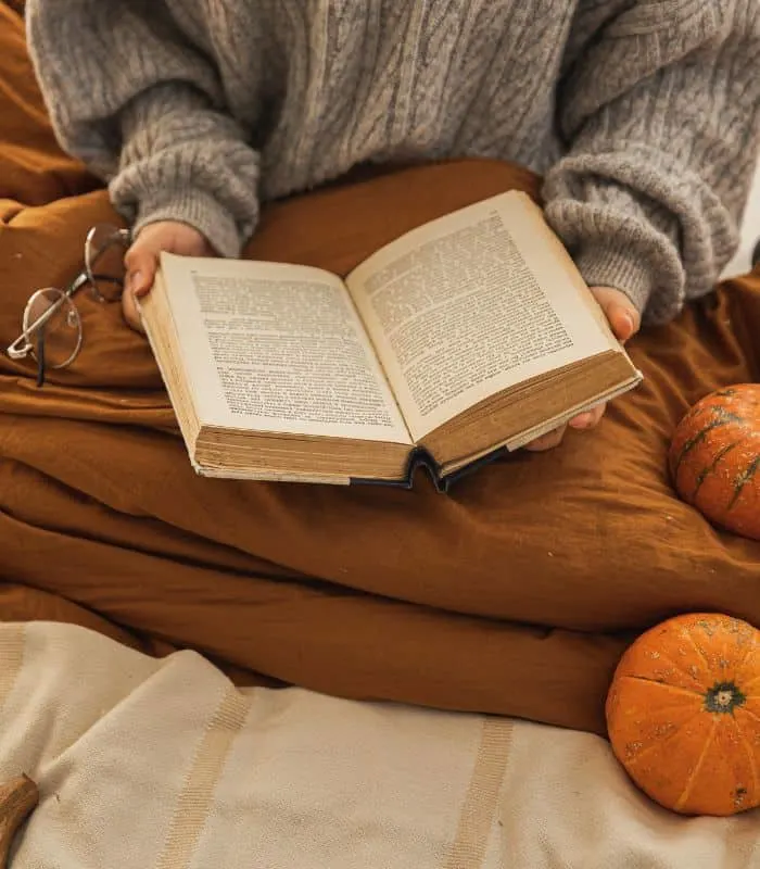 woman reading one of the Adventure Fiction Books For Adults next to some pumpkins