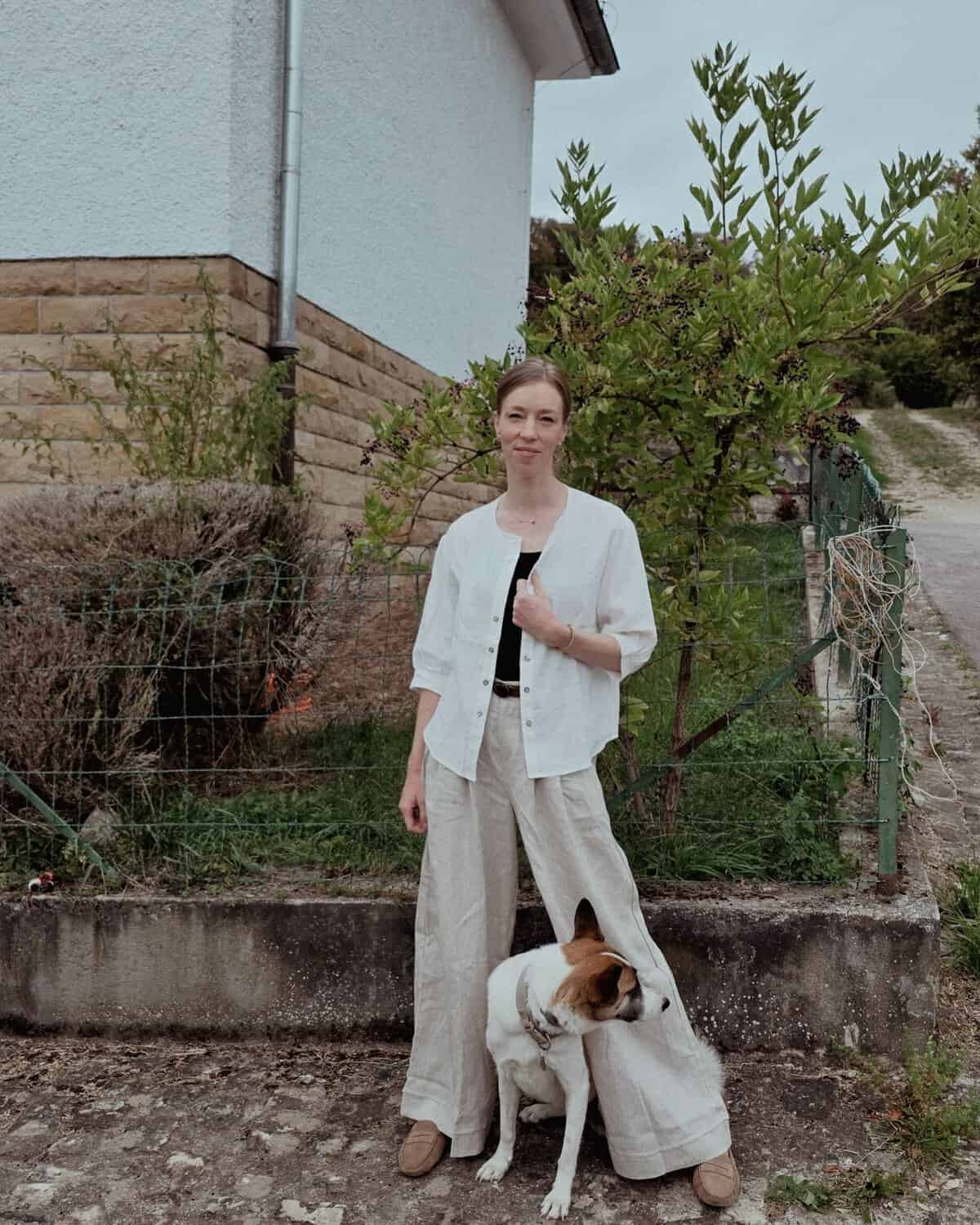 Travel Blog Why I Switched to Linen for Travel Lintico Discovery | Paulina | Woman wearing a black shirt, white top, and linen pants with a dog near a garden at the background